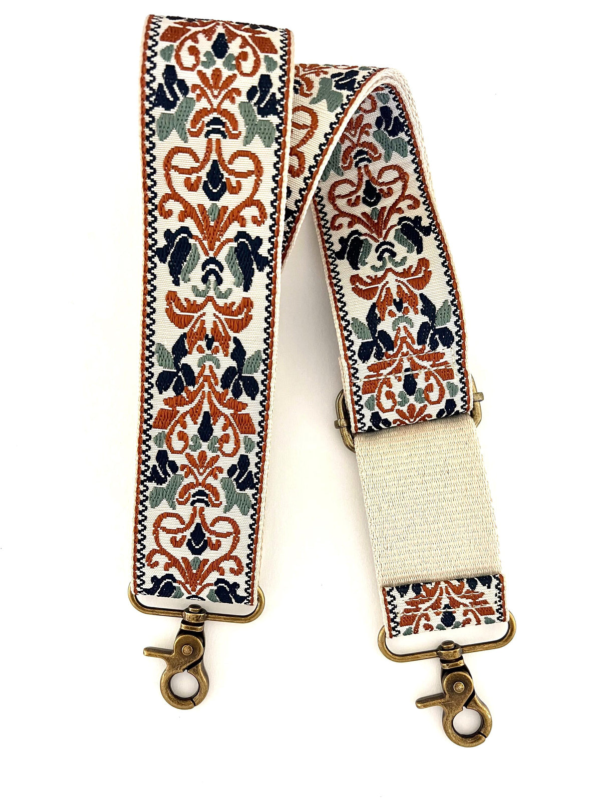 A woven fabric shoulder strap with an ornate damask pattern in rust orange, navy blue, sage green, and cream, featuring brass-toned metal swivel clips and an adjustable cream elastic section.